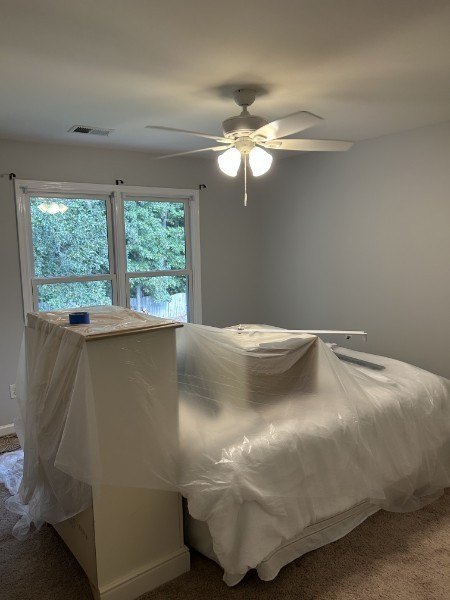 Bedroom with freshly painted light gray walls, the bed and dresser covered in plastic