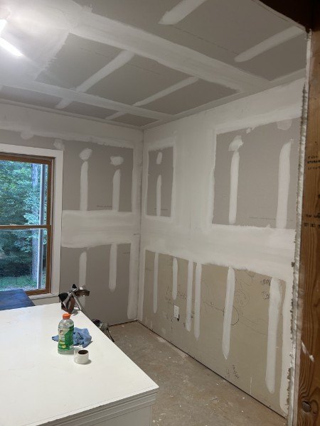 Taped and mudded drywall in a room with a window, before painting