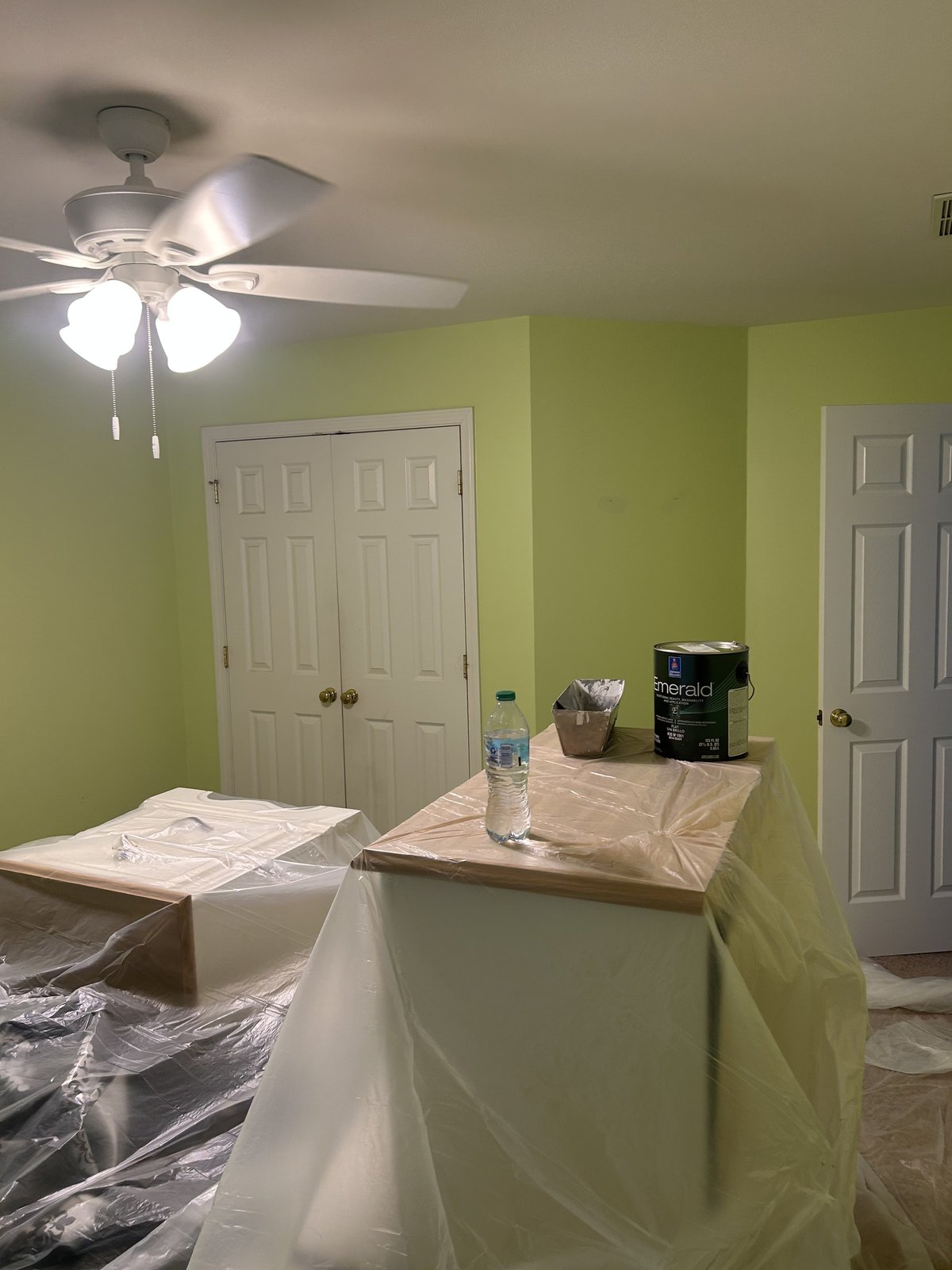 Bedroom with bright green walls before repainting, the furniture covered in plastic sheeting