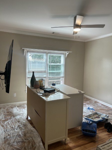 Freshly painted gray bedroom with white trim, a window and a ceiling fan, drop cloths on the floor