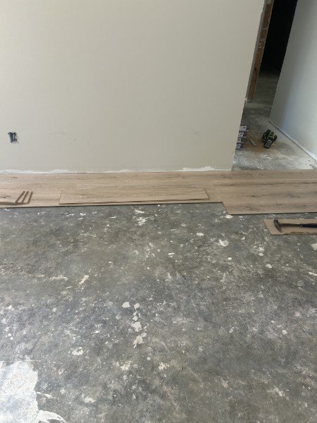 First rows of new plank flooring laid along a wall over concrete